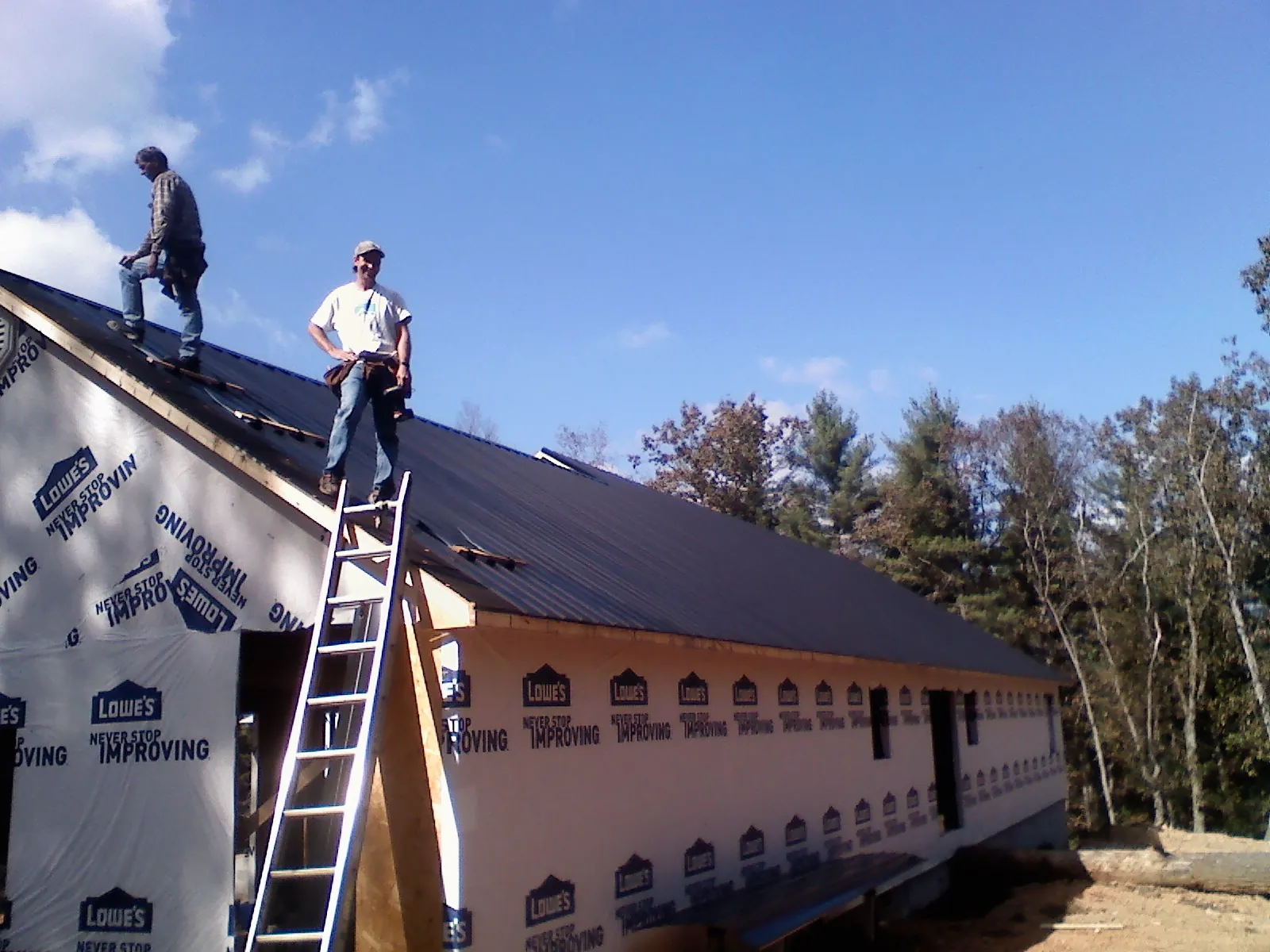 Two roofers standing on a long dark metal roof over a wrapped building in Fairfax